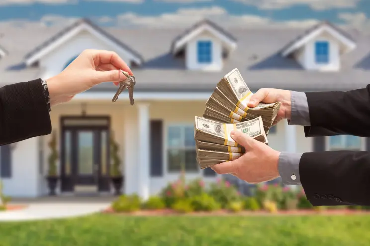 A person handing over house keys while receiving cash, with a house in the background in Fayetteville.
