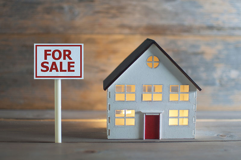 A miniature house with a "For Sale" sign.