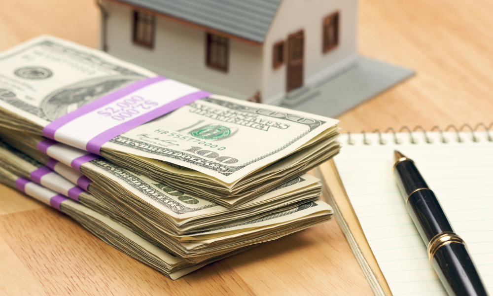 A miniature house placed next to money, a pen, and a notebook, representing selling a property in Gastonia for cash.