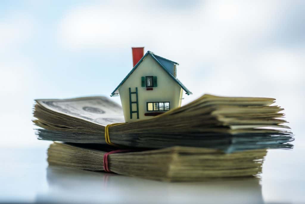 A miniature house placed on top of cash, representing selling a Charlotte home fast for cash in any condition.