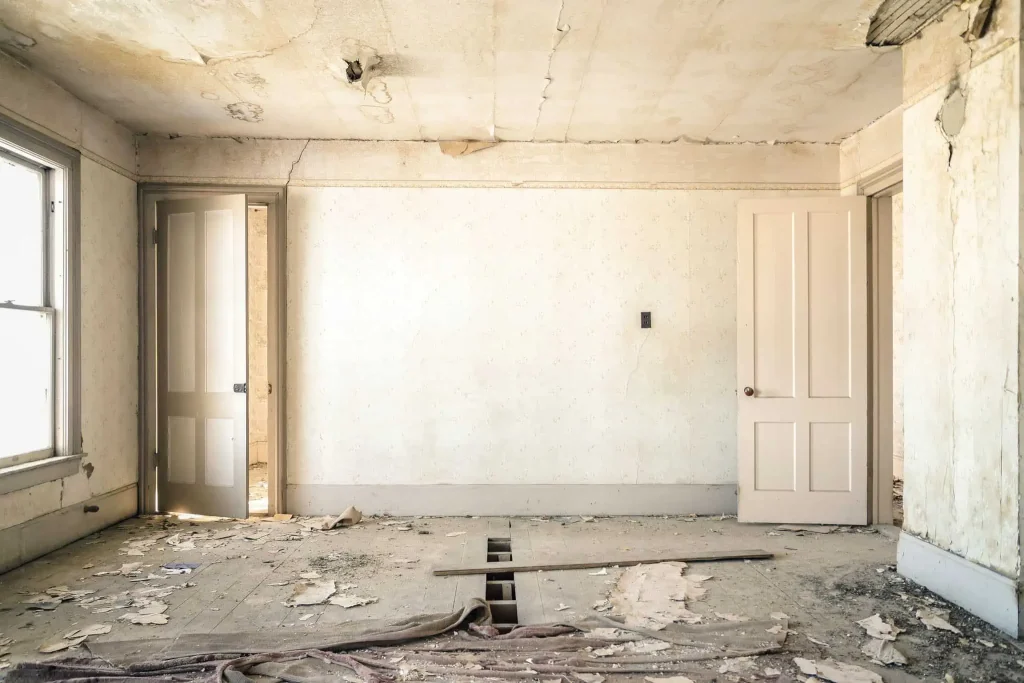 An interior of a house in Greensboro with a damaged floor, window, ceiling, and door, indicating the need for major repairs.