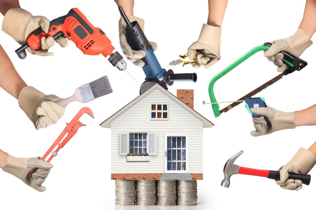 A house placed above coins surrounded by hands holding tools for repairing a house.