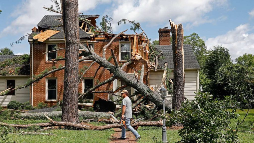 A storm-damaged house in Charlotte with a fallen tree and visible structural damage.